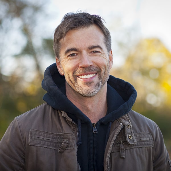 A man smiling in a park wearing a jacket